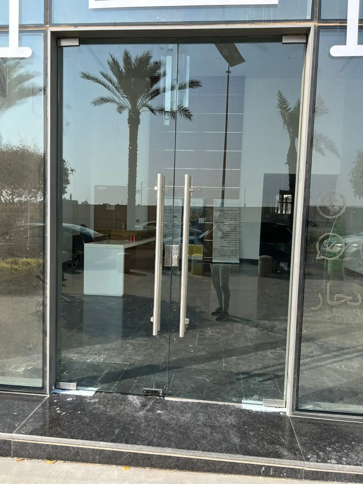 باب زجاجي مزدوج للمدخل الرئيسي بمقابض ستانلس ستيل طويلة في واجهة مبنى تجاري.