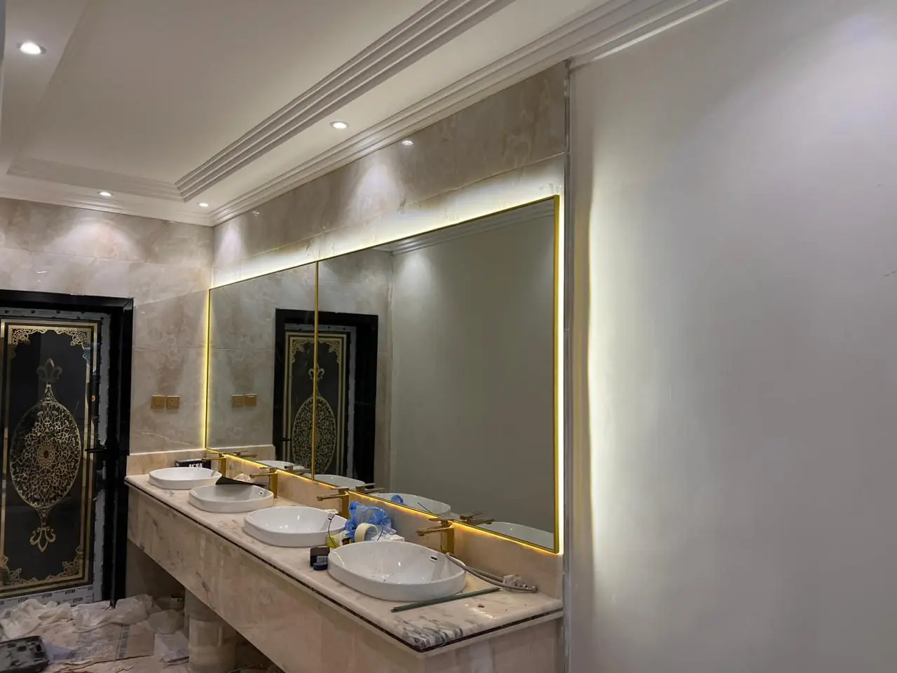 مرايا حمام عرضية بإطار ذهبي وإضاءة ليد خلفية فوق مغاسل رخامية فاخرة في جدة.