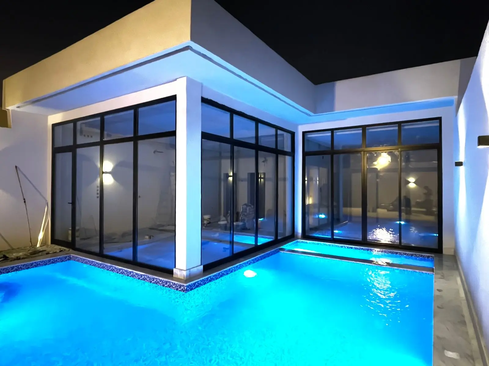 واجهات زجاجية كبيرة وإطارات سوداء يطل على مسبح بإضاءة زرقاء ليلية.