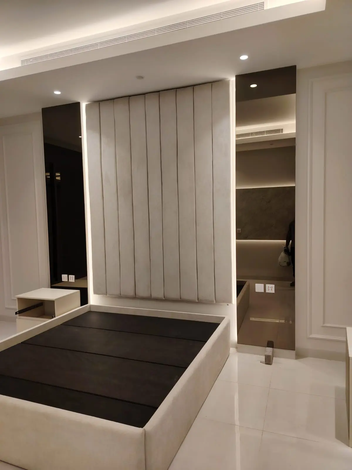 ديكور غرفة نوم مودرن يضم مرايا طولية بلون فاميه على جانبي خلفية سرير منجدة مع إضاءة ليد.