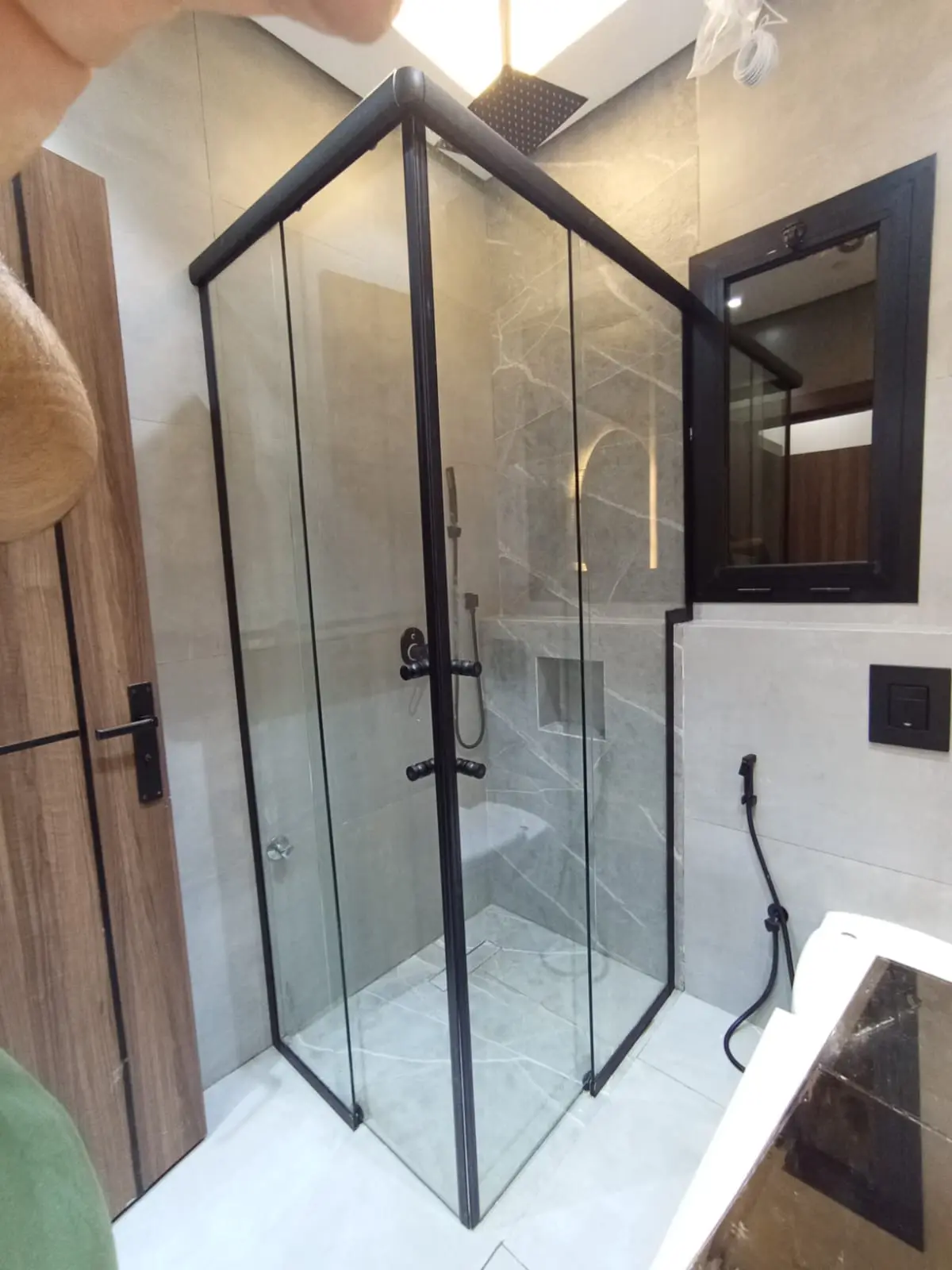 كبينة شاور زاوية زجاجية بإطار ألمنيوم أسود كامل ومقابض دائرية في حمام مودرن.